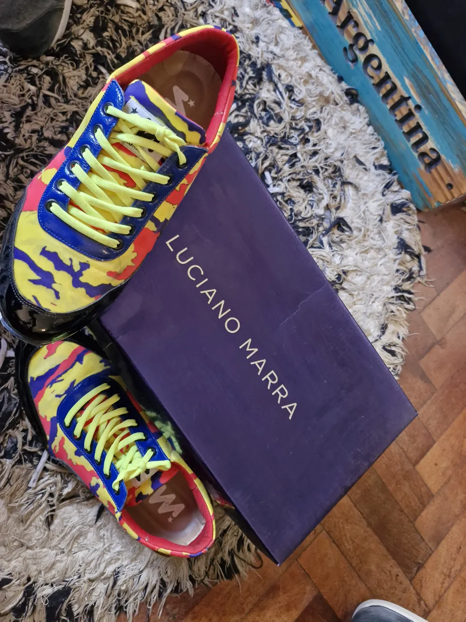 Zapatillas deportivas Luciano Marra con diseño camuflado en amarillo, azul y rojo. Cordones amarillos y detalles en negro. Ideales para un look urbano y moderno.