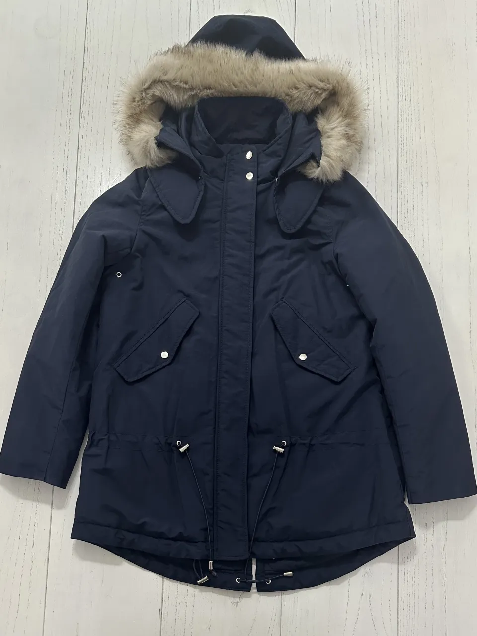 Campera azul marino con capucha forrada en piel sintética. Posee bolsillos frontales con solapa y botones a presión. Tiene cordón ajustable en la cintura y cierre principal con botones a presión y cierre.