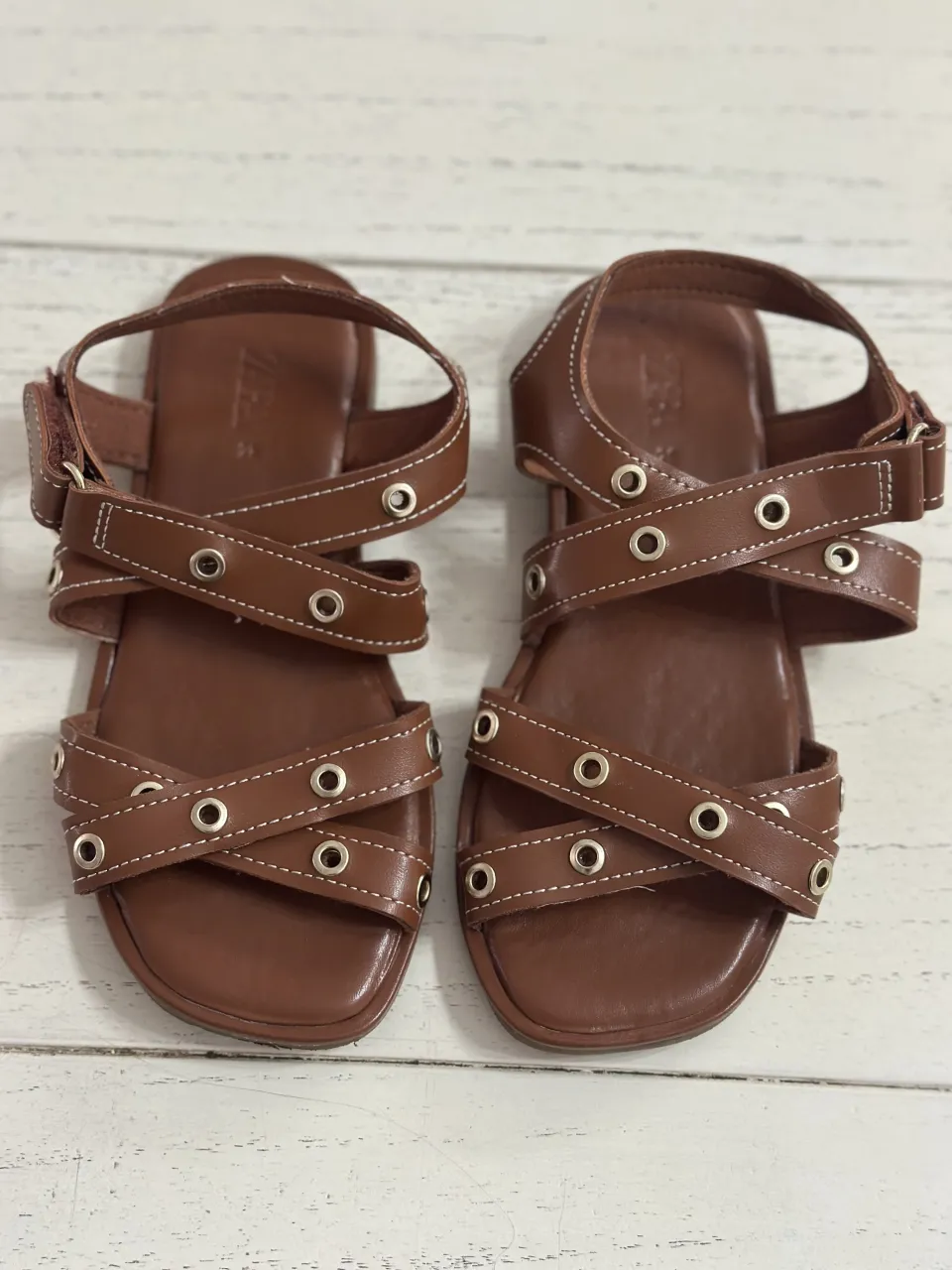 Sandalias marrones de tiras cruzadas con detalles de ojales y costuras blancas.