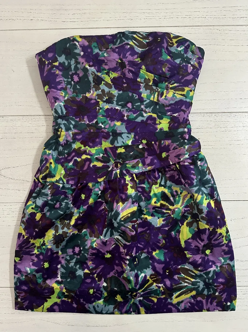 Vestido strapless estampado floral en tonos violeta, verde y amarillo. Posee un lazo en la cintura y fruncido en el busto.