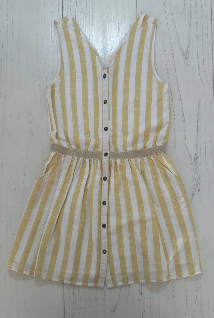 Vestido a rayas verticales amarillas y blancas, con cuello en V y botones en la parte delantera. Posee cintura elastizada con detalle de brillos y bolsillos laterales.