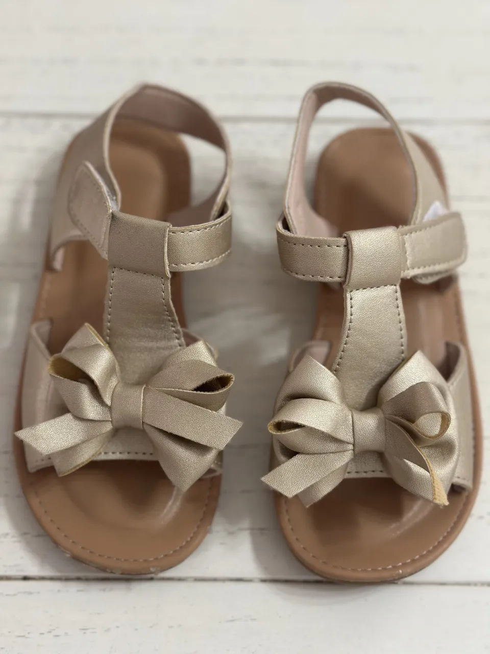 Sandalias doradas con lazo en la punta. Tienen abrojo en la tira del tobillo.