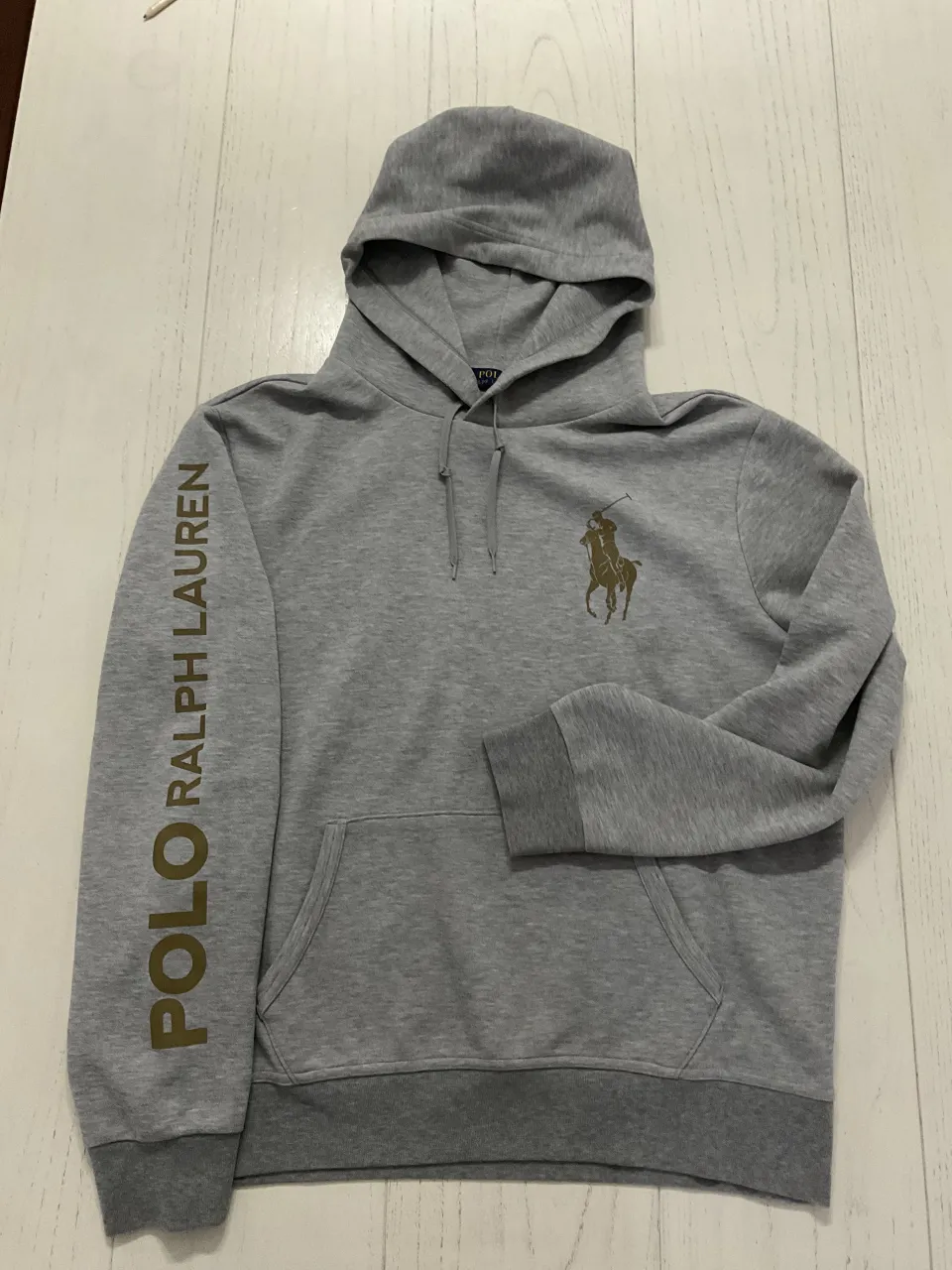 Buzo gris con capucha y cordones. Estampa del logo de la marca y nombre de la marca en una de las mangas.