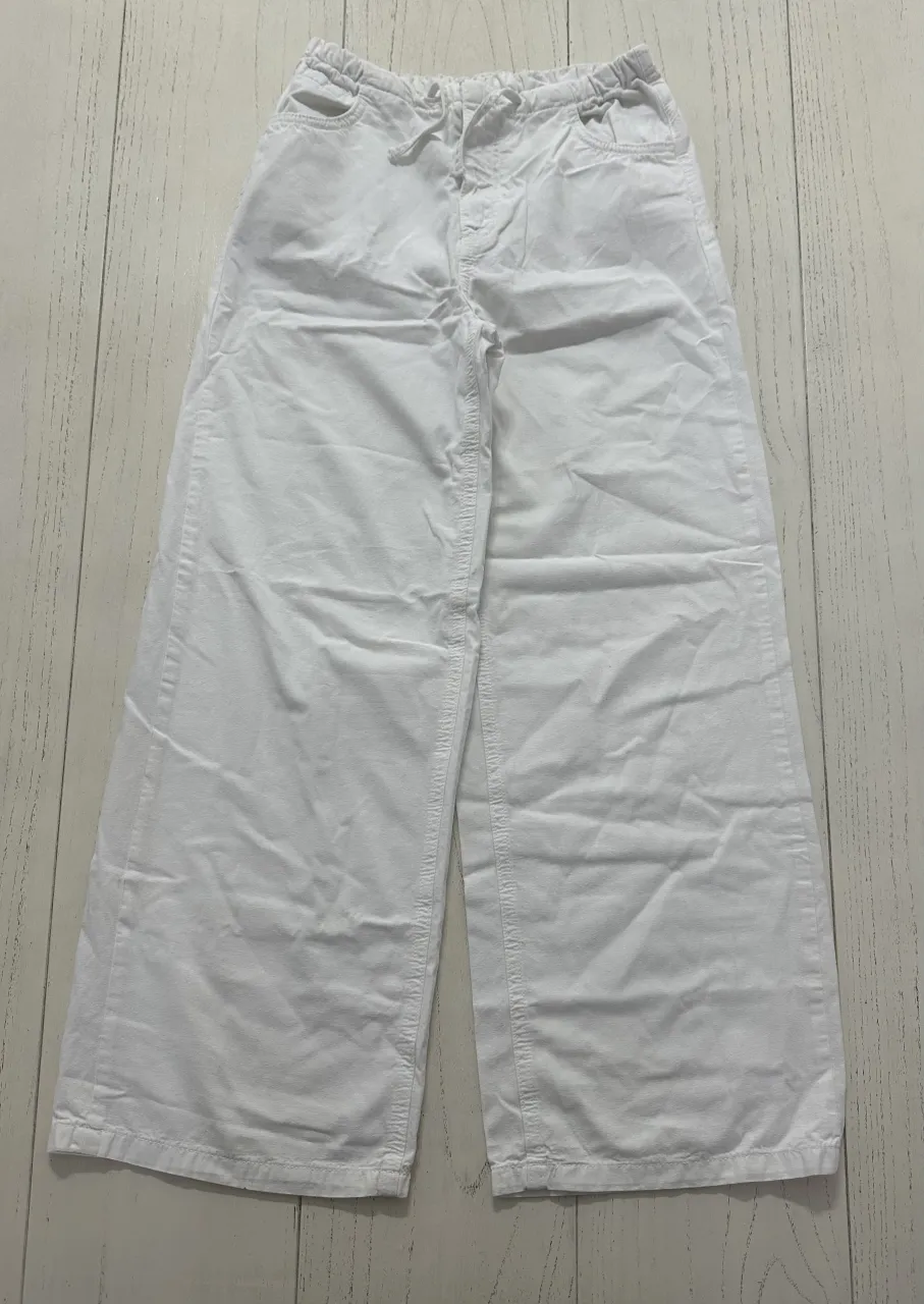 Pantalón blanco de tela con cintura elástica y cordón. Tiene bolsillos delanteros y traseros.