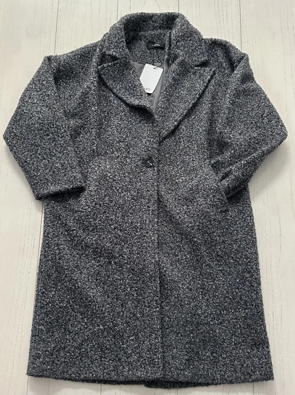 Abrigo largo de paño gris con cuello solapa y un botón al frente. Posee bolsillos laterales.