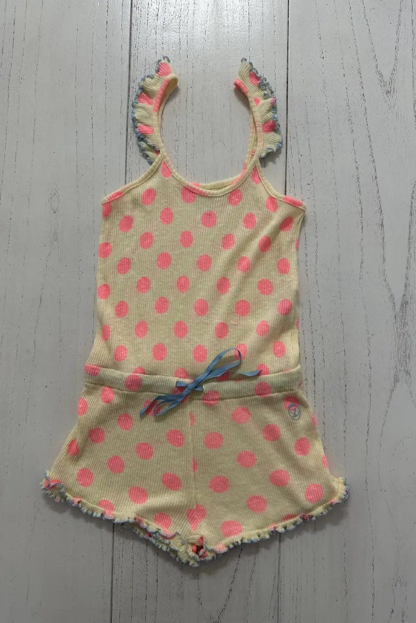 Mono corto de algodón amarillo con estampa de lunares rosas. Tiene volados en los breteles y en el borde inferior de los shorts. Posee un lazo de cinta azul en la cintura.
