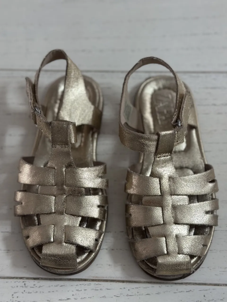 Sandalias doradas con tiras entrecruzadas y hebilla ajustable.