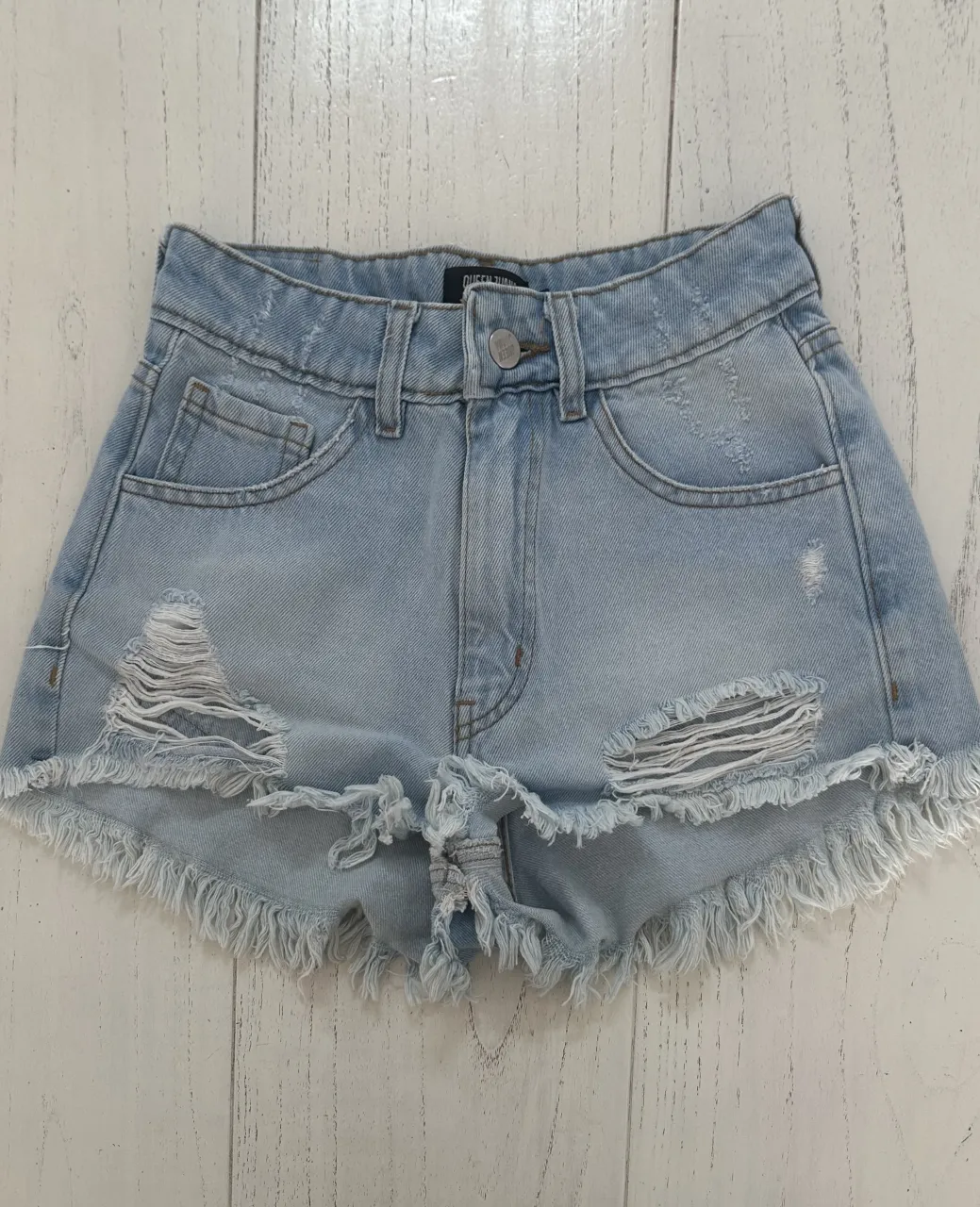 Shorts de jean tiro alto con roturas y flecos en el ruedo. Detalle de roturas en los bolsillos delanteros y trasero.