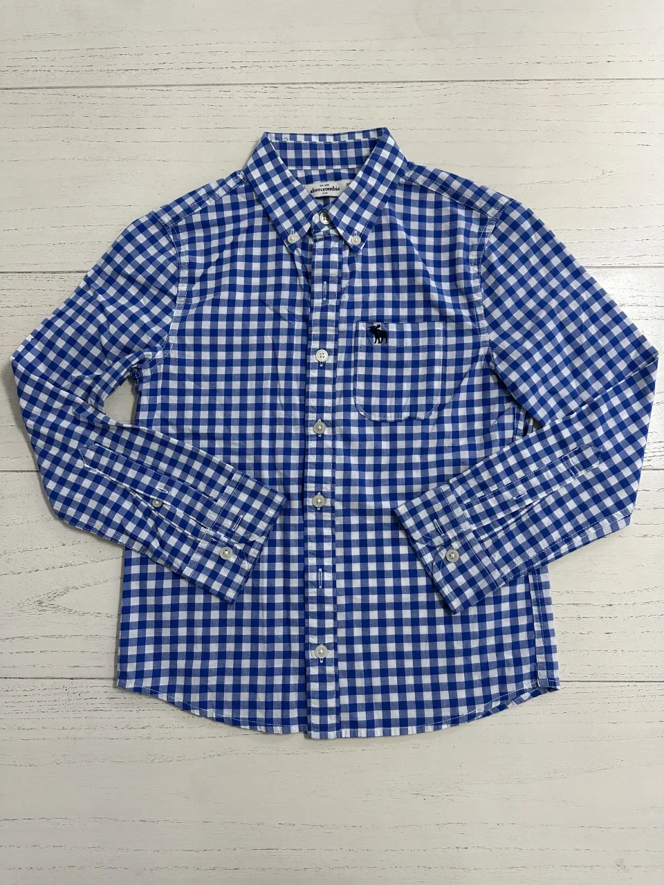 Camisa a cuadros de manga larga con botones al frente y bolsillo en el pecho. Presenta un pequeño bordado de un alce en el bolsillo.