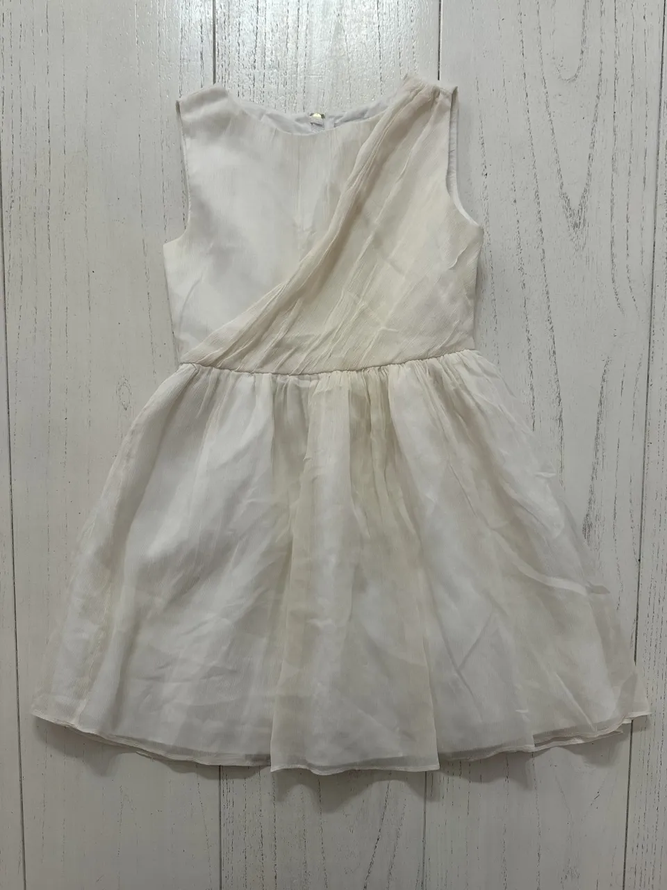 Vestido blanco sin mangas con detalle drapeado en el frente y falda con pliegues. Cierre en la espalda.