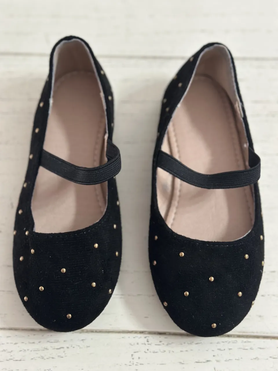 Zapatillas negras con tachas doradas y tira elástica.