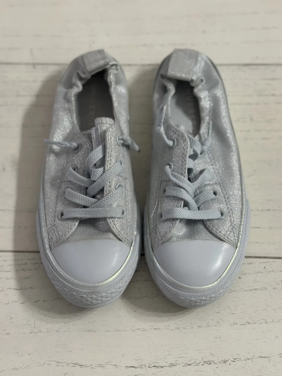 Zapatillas plateadas con cordones y detalles brillantes. Diseño tipo slip-on con elástico en el talón.