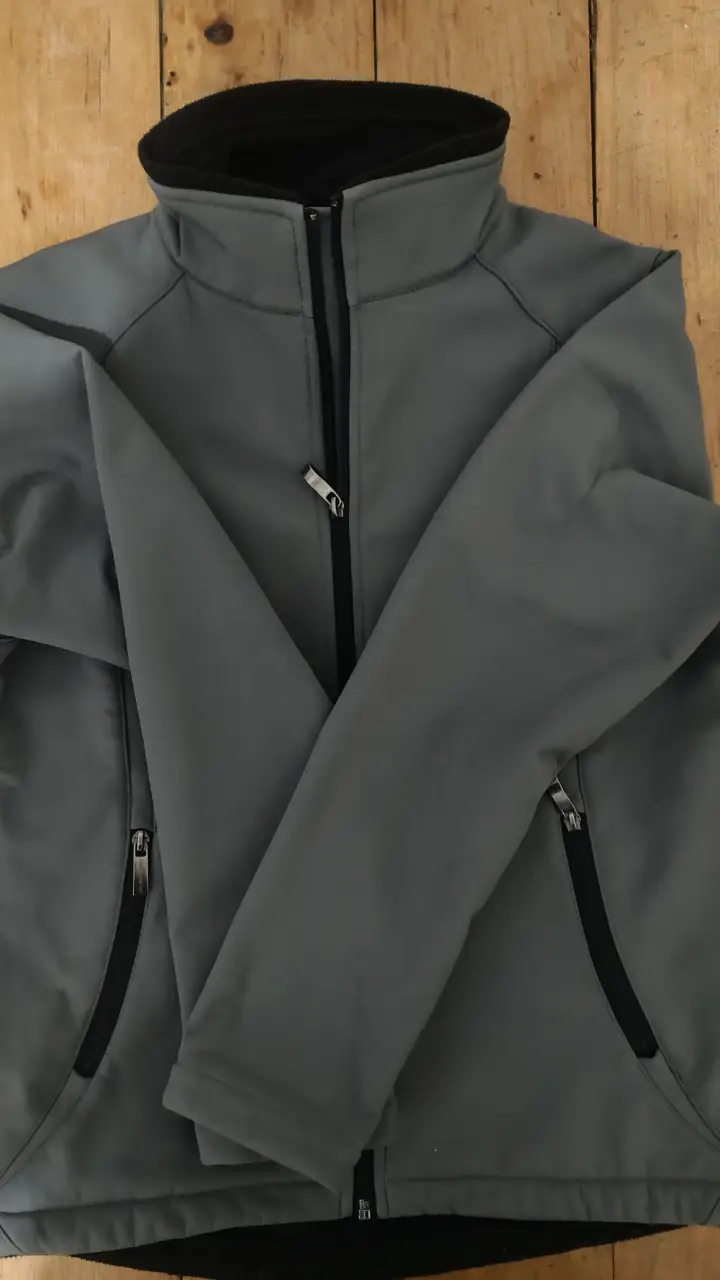 Campera softshell gris para mujer, con cierre y bolsillos con cierre. Cuello alto y detalles en negro. Ideal para el día a día.