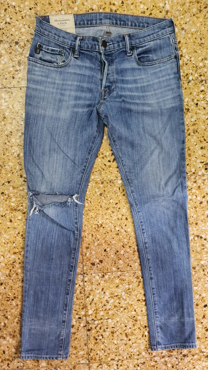 Jeans de hombre Abercrombie & Fitch, azul gastado con roturas en la rodilla. Talle 33x32, corte recto, ideal para un look casual y moderno.