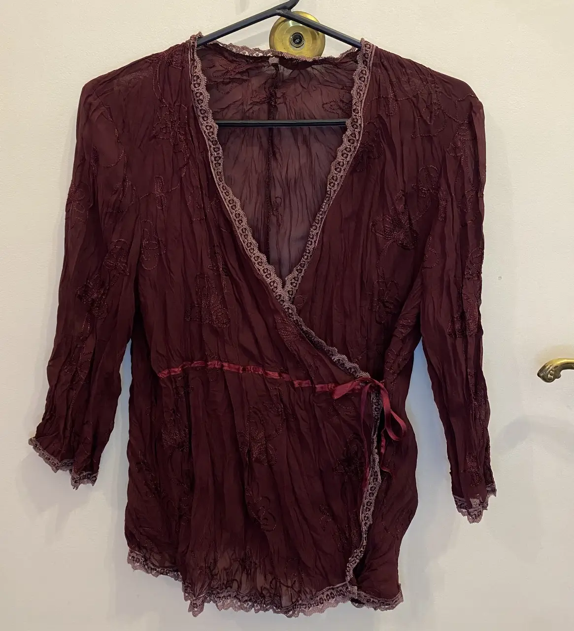 Blusa en color borgoña con bordados florales. Diseño cruzado con lazos para ajustar y detalles de encaje en los bordes. Ideal para un look bohemio y elegante.