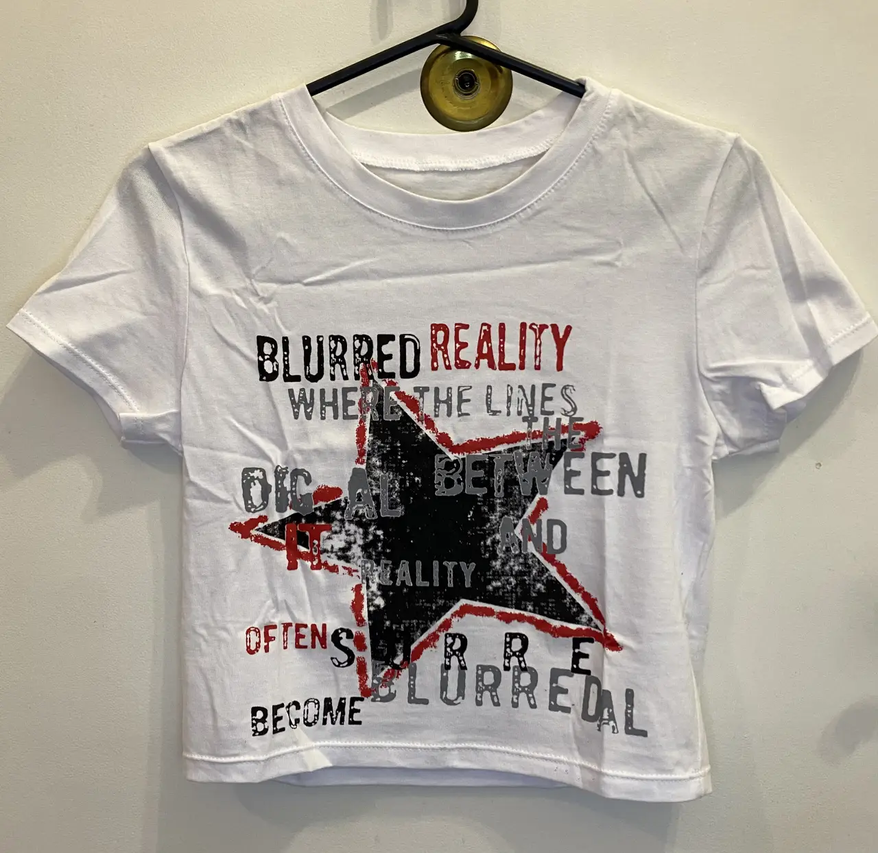 Remera blanca con estampado de estrella negra y detalles en rojo. Diseño con texto "BLURRED REALITY". Medidas aproximadas (tomadas en plano): 39cm de ancho, 42cm de largo