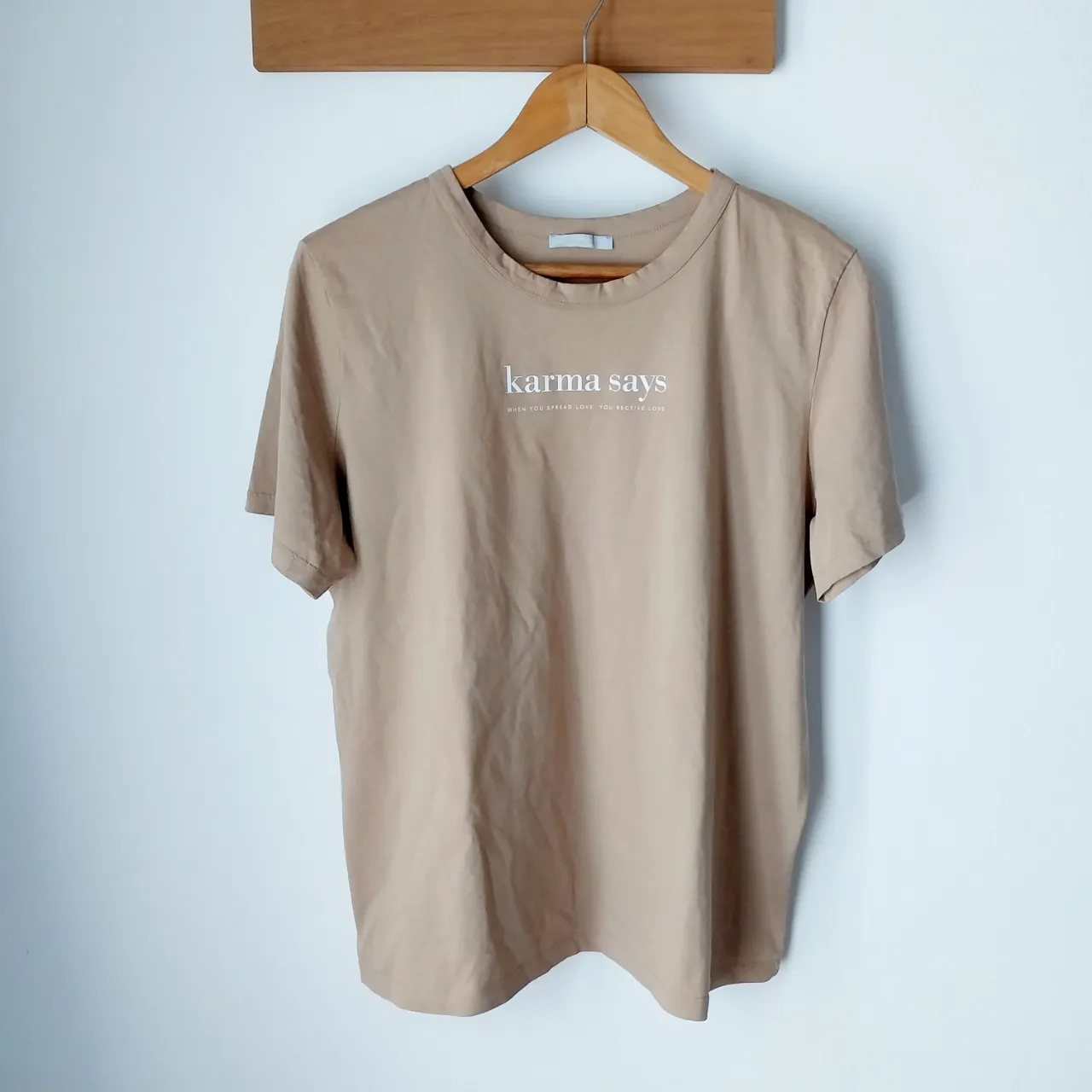 Remera de algodón color tiza con estampa "karma says" en blanco. Cuello redondo y mangas cortas. Ideal para un look casual y relajado.