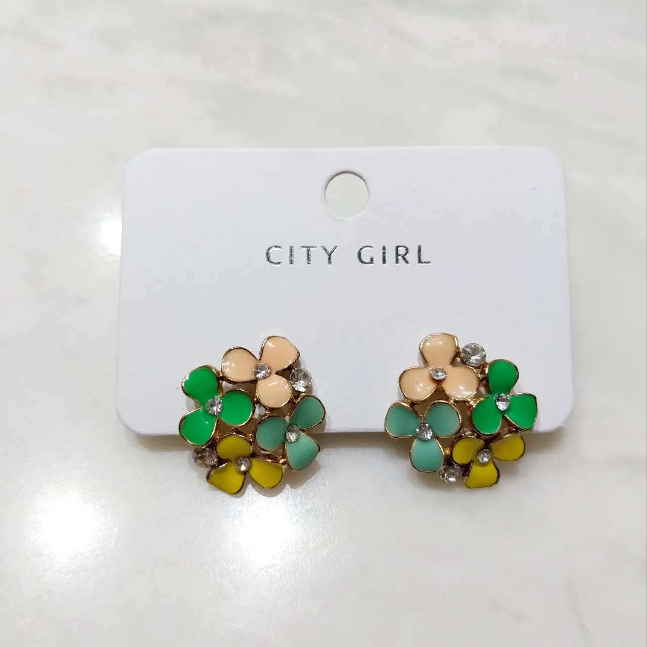 Aros con forma de flores en tonos verde, rosa pálido, verde agua y amarillo, con detalles de strass en el centro de cada flor. Vienen montados sobre una tarjeta blanca con el logo "CITY GIRL".