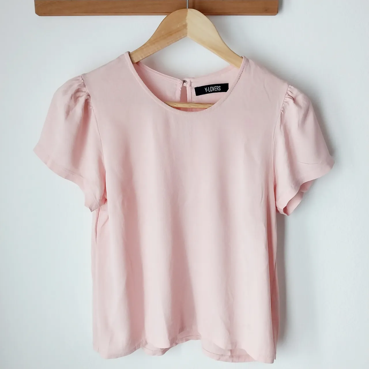 Remera rosa de manga corta con cuello redondo y detalle de frunces en los hombros. Cierre en la espalda.