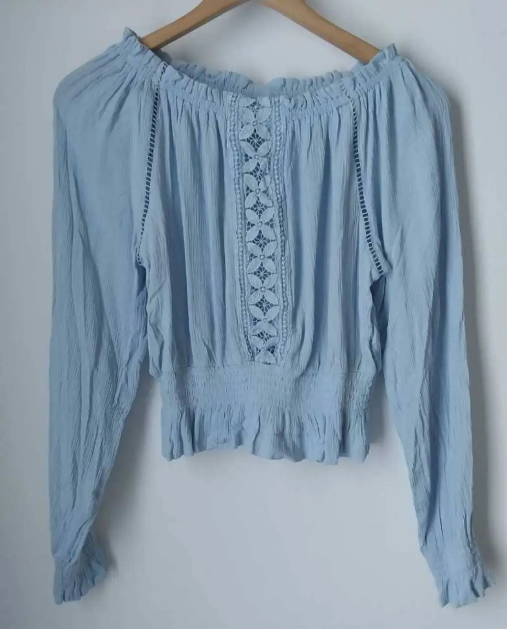 Blusa celeste con detalles de encaje en el centro y en los laterales. Tiene mangas largas y un corte a la cintura con elástico. Ideal para un look bohemio y fresco.