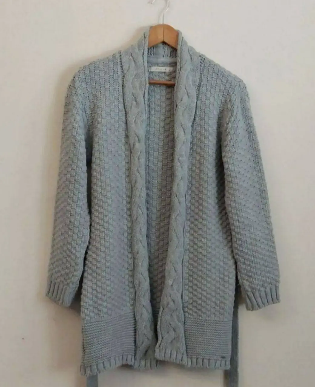 Cardigan de tejido grueso en color gris, con diseño de trenzas en la parte central y cinturón para ajustar. Ideal para un look casual y abrigado.