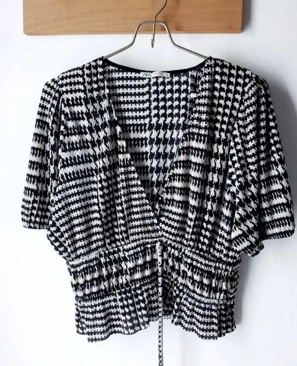 Blusa de mujer con estampado geométrico en blanco y negro. Diseño con escote en V y mangas cortas amplias. Corte a la cintura con detalle fruncido. Ideal para un look elegante y moderno.