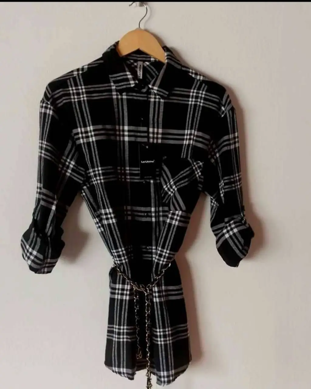 Camisa a cuadros en blanco y negro, con mangas largas que se pueden arremangar. Incluye un cinturón con cadena para ajustar la cintura. Ideal para un look casual y moderno.