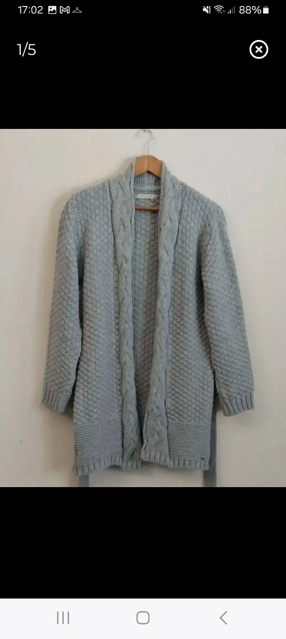 Cardigan largo de tejido grueso, color gris. Con diseño de trenzas en la parte delantera y mangas. Incluye cinturón para ajustar en la cintura. Ideal para un look casual y abrigado.