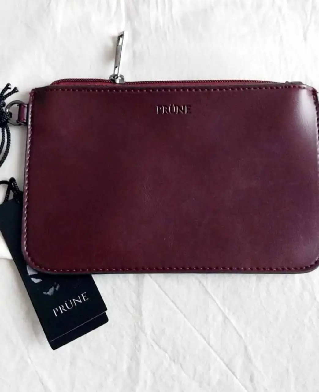 Cartera PRUNE de cuero color borravino, con cierre y logo de la marca. Ideal para llevar tus esenciales con estilo.