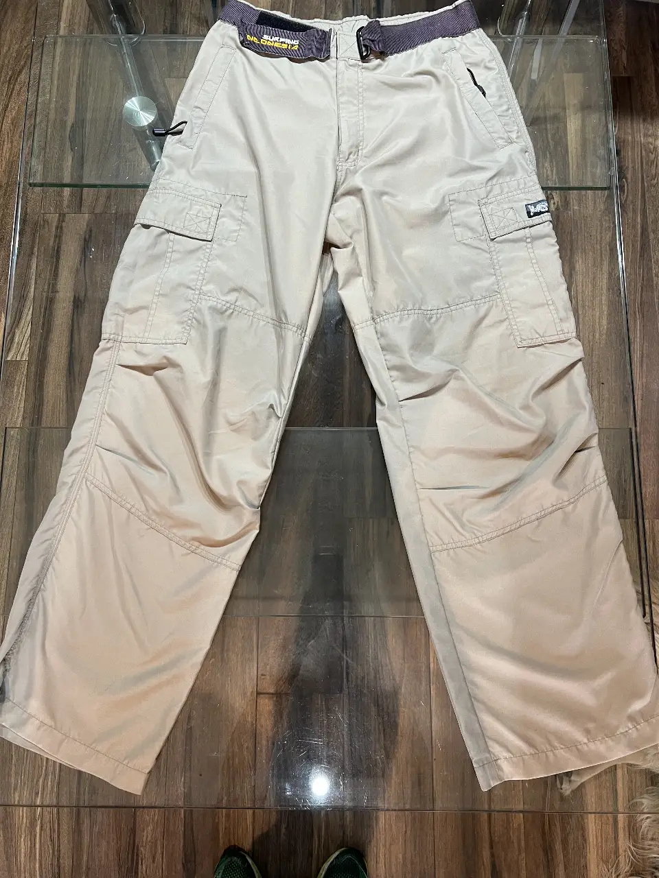 Pantalón cargo color crudo para hombre. Confeccionado en poliéster, talle 40. Posee múltiples bolsillos y cinturón con detalles en amarillo. Ideal para un look utilitario y casual.