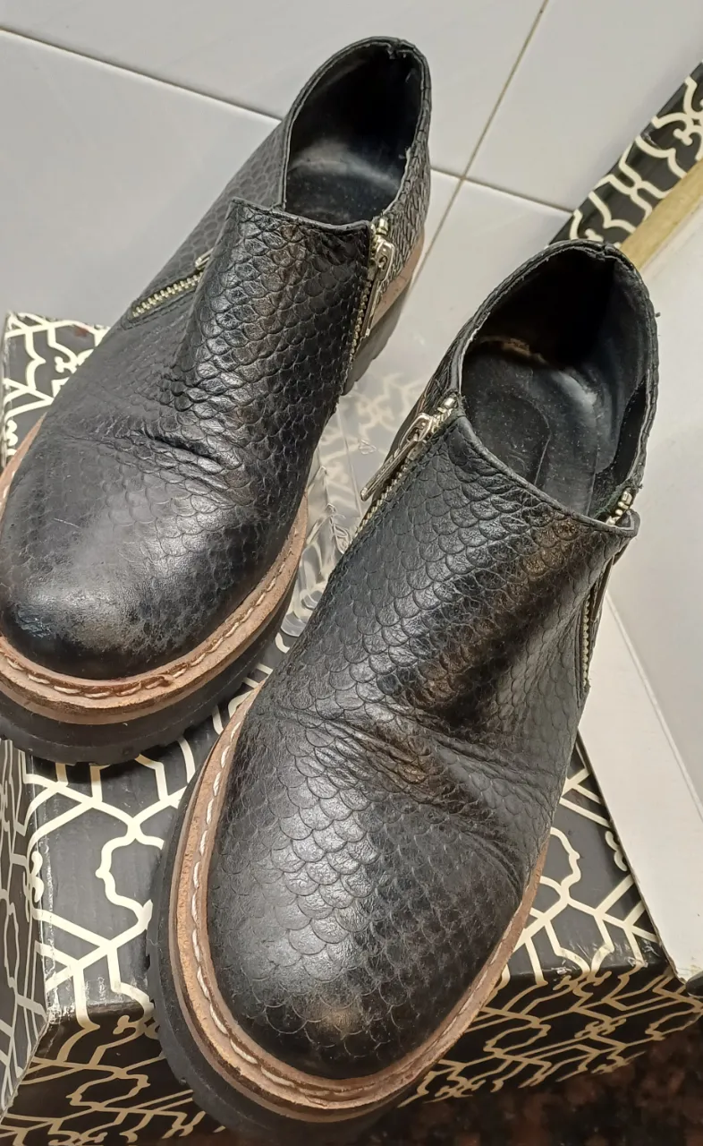 Botines negros con textura de reptil y cierre en el lateral. Suela gruesa y detalles en marrón claro. 