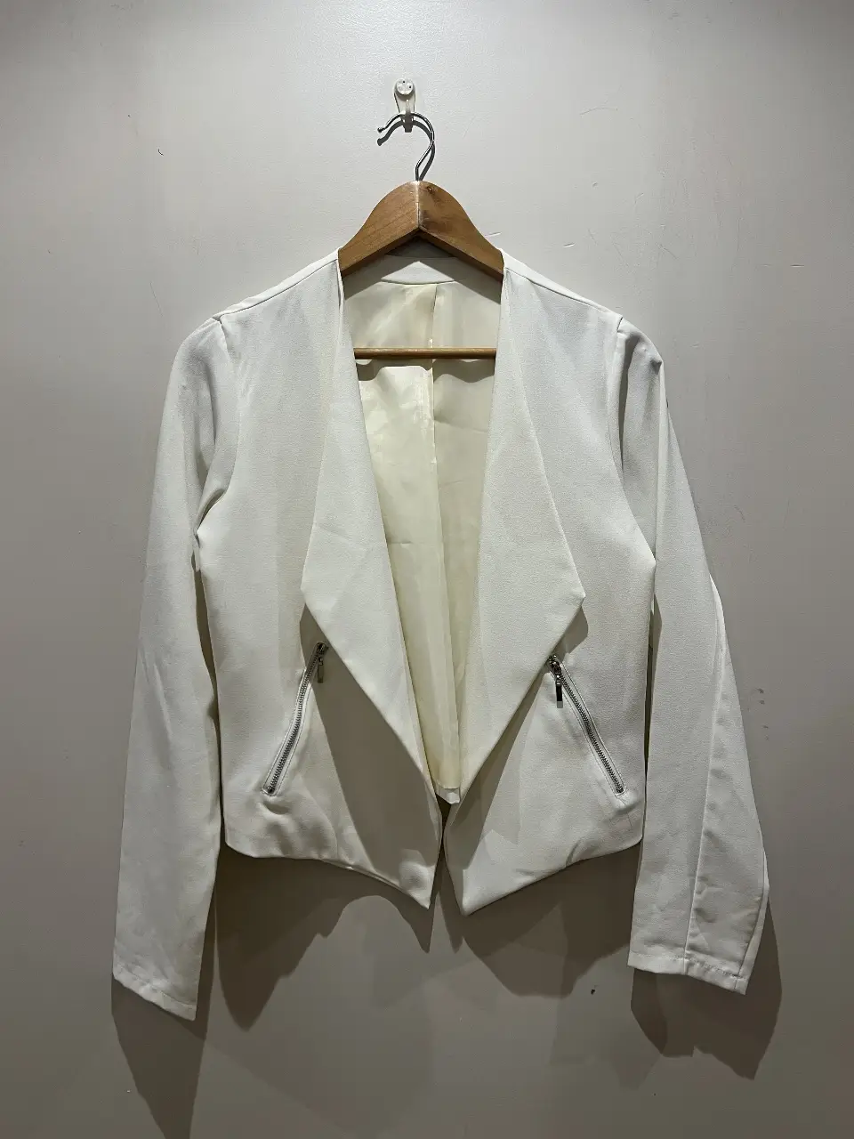 Blazer blanco de mujer, con solapas amplias y cierre con cremalleras en los bolsillos. Ideal para un look elegante y moderno.