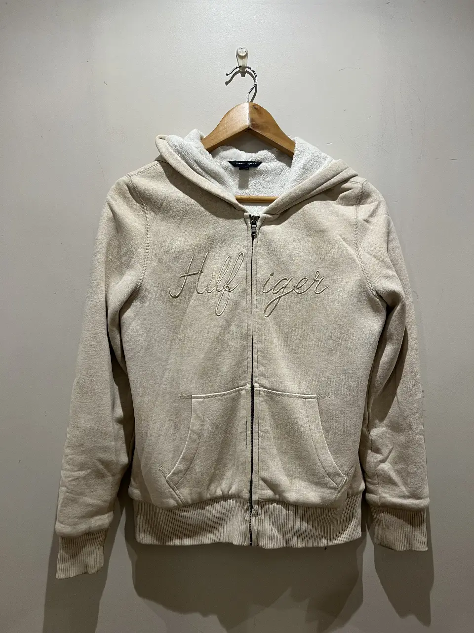 Buzo con cierre Tommy Hilfiger para mujer, color crudo, con capucha y bolsillo tipo canguro. El logo de la marca está bordado en el frente. Talle S.