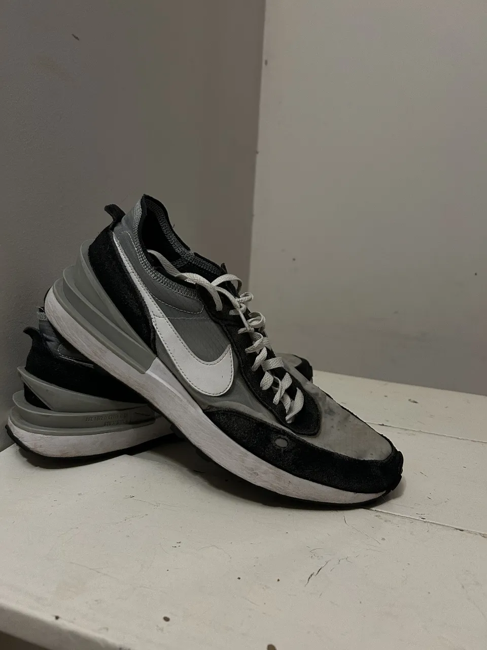 Zapatillas deportivas Nike Waffle, ideales para uso diario. Diseño moderno en tonos grises y negros con detalles blancos.