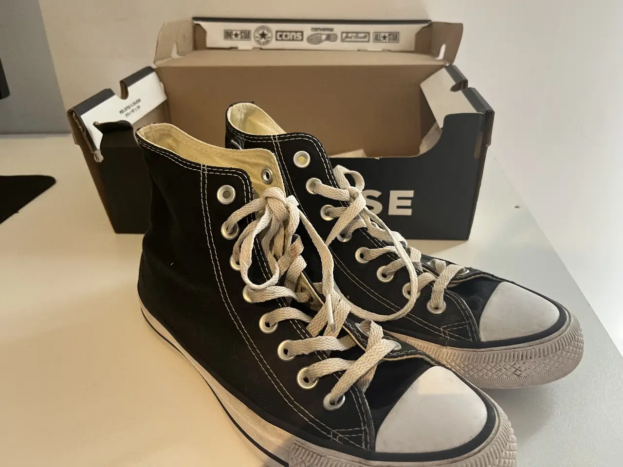 Zapatillas Converse All Star negras de caña alta, con puntera blanca y cordones. Un clásico atemporal para un look casual y urbano.
