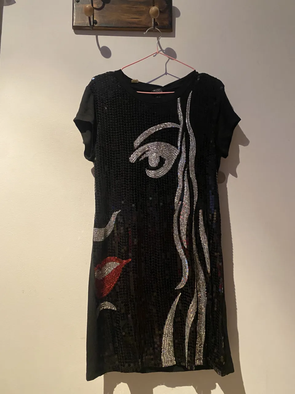 Vestido negro con lentejuelas y aplique de rostro abstracto en plateado y labios rojos.