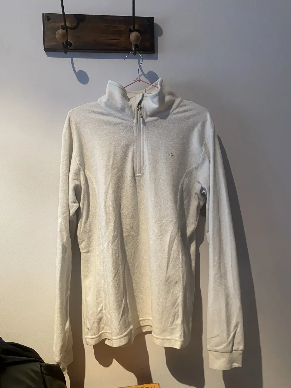 Buzo blanco de cuello alto con cierre parcial en el frente. Presenta un pequeño logo bordado en el pecho.