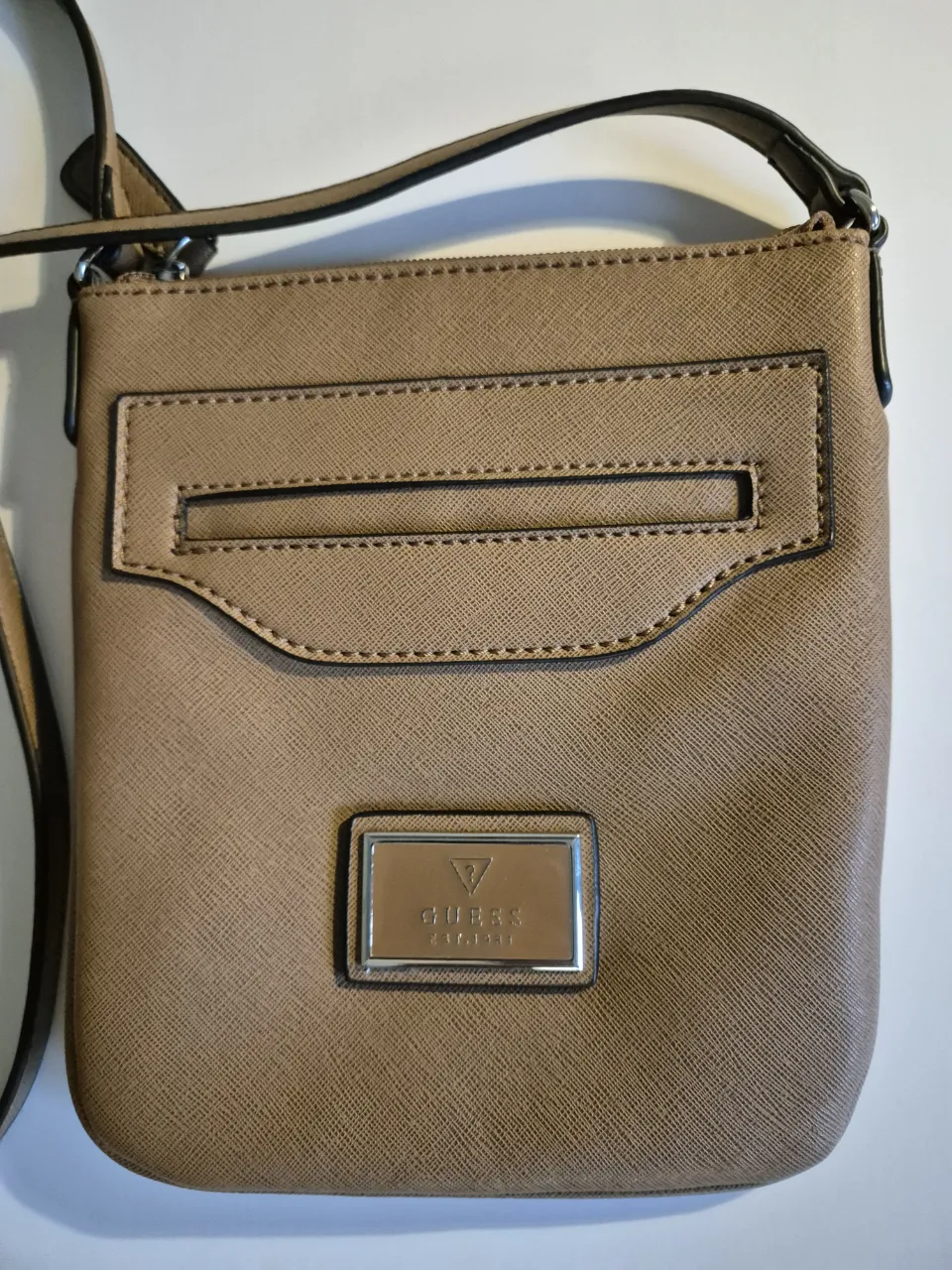 Bandolera Guess color marrón, con correa ajustable. Diseño elegante y práctico, ideal para llevar tus esenciales con estilo. Cuenta con un bolsillo frontal y un interior espacioso con forro estampado.