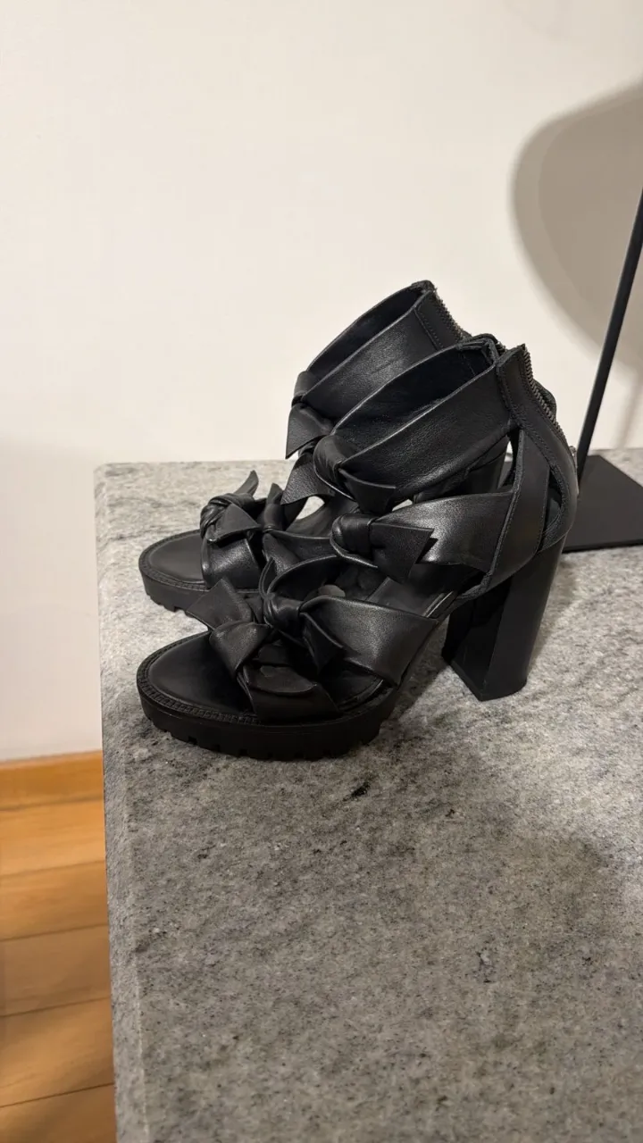 Sandalias negras de cuero con tiras anudadas en la capellada y cierre en el talón. Taco grueso y plataforma.
