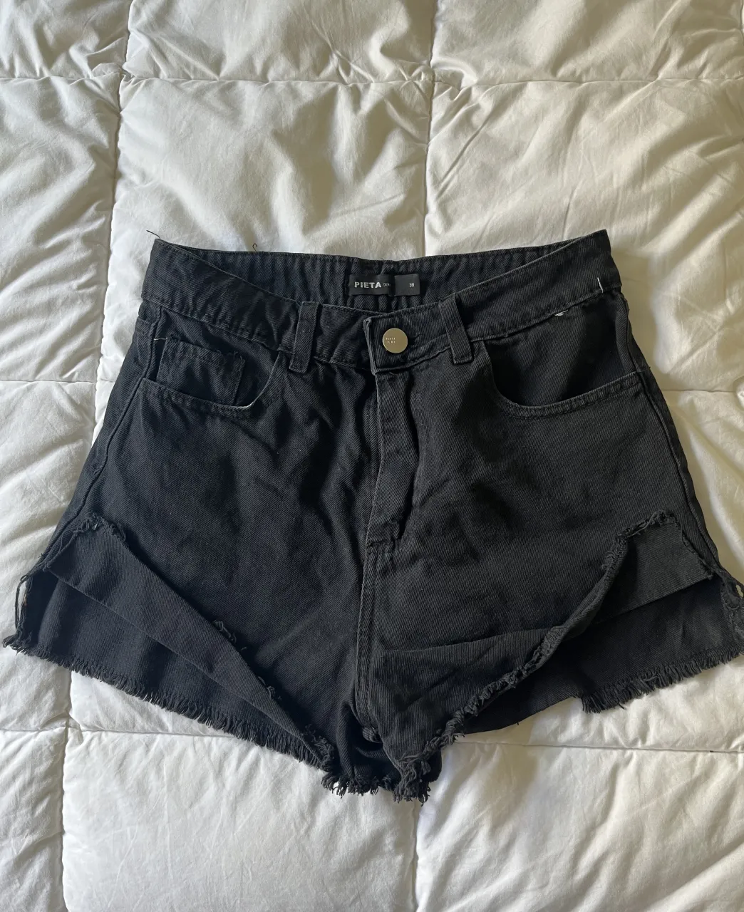 Shorts de jean negros con roturas y detalles deshilachados en los bordes.