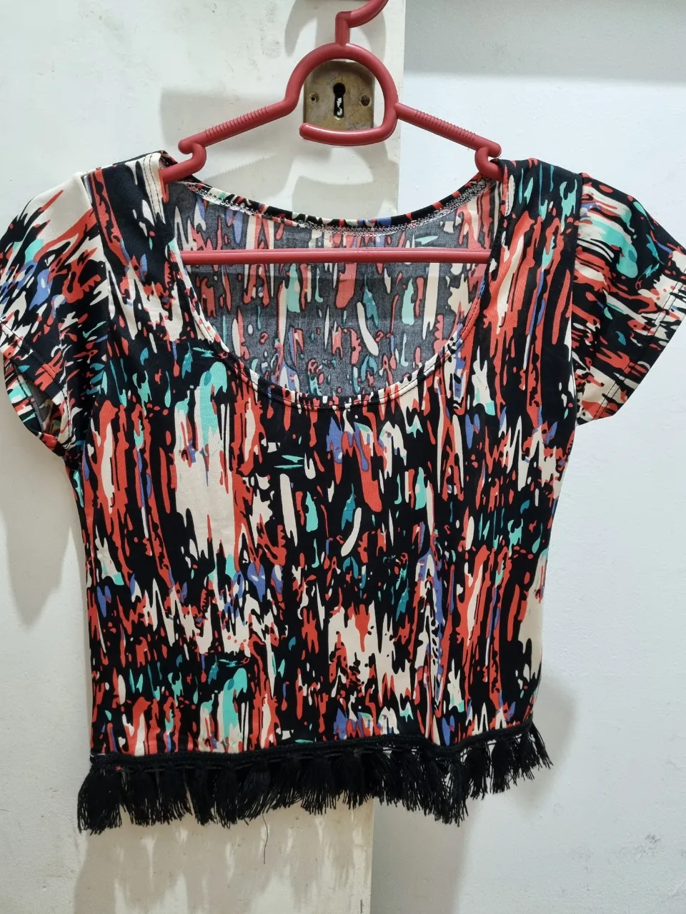 Top de mujer con estampado abstracto en tonos vibrantes. Diseño con cuello redondo y detalle de flecos en el bajo. Ideal para un look casual y moderno.