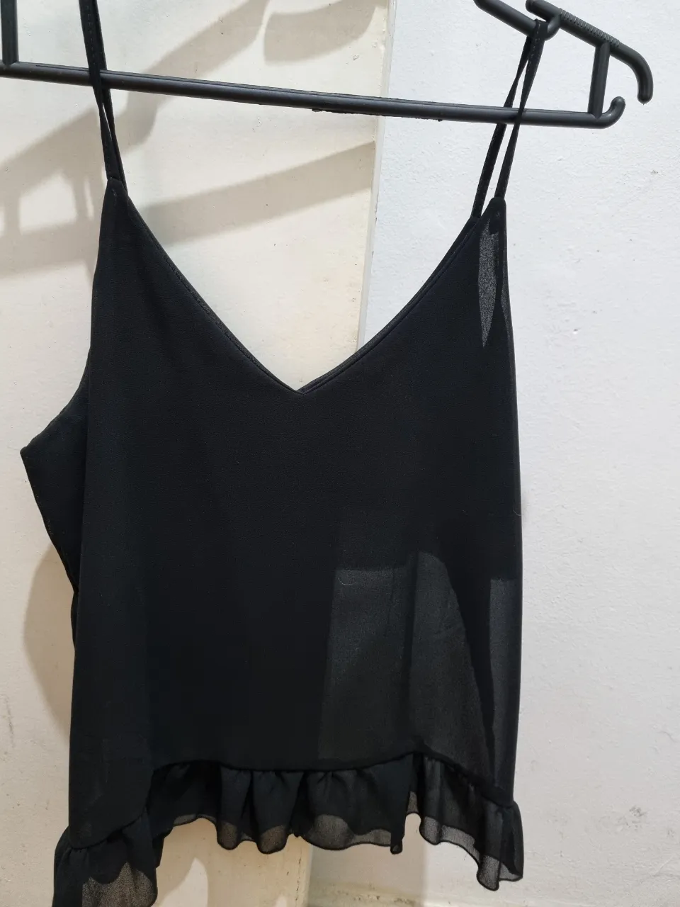 Top negro con breteles finos y escote en V, con volados en el borde inferior. Ideal para un look elegante y fresco.