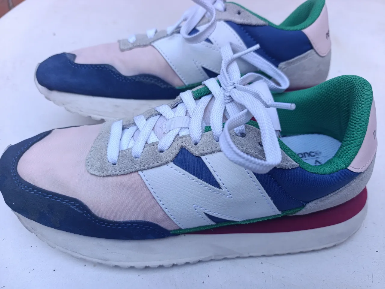 Zapatillas New Balance 237 con cordones blancos. Combinan paneles de gamuza y tela en tonos rosa pálido, azul marino, blanco y verde.
