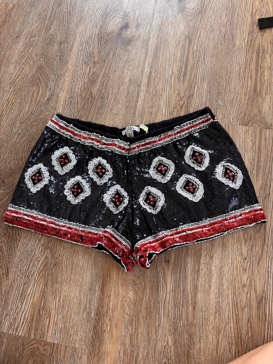 Shorts Zara negros con lentejuelas y bordados de rombos en blanco y rojo. Detalle mostacillas y lentejuelas rojas en el ruedo. Ideales para un look festivo y llamativo.