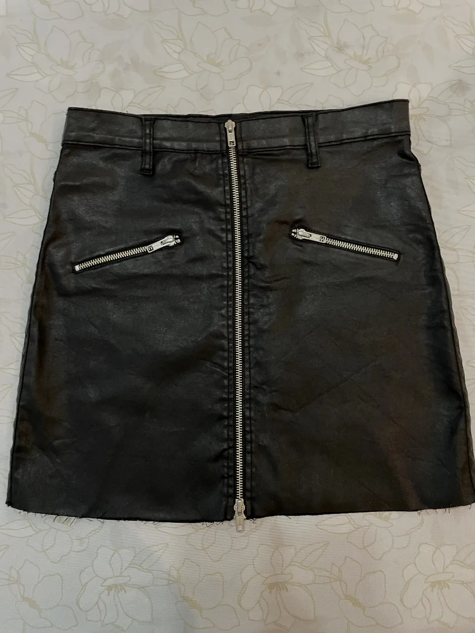 Pollera negra efecto cuero con cierre frontal. Apliques de cierres adelante, y bolsillos traseros. Marca CHER. La tela es ligeramente elastizada. Está impecable, no tiene ningún detalle! El largo es un poquito más que una minifalda, queda por encima de la rodillas. Es muy original, efecto cuero y a la vez efecto jean. Talle 28.