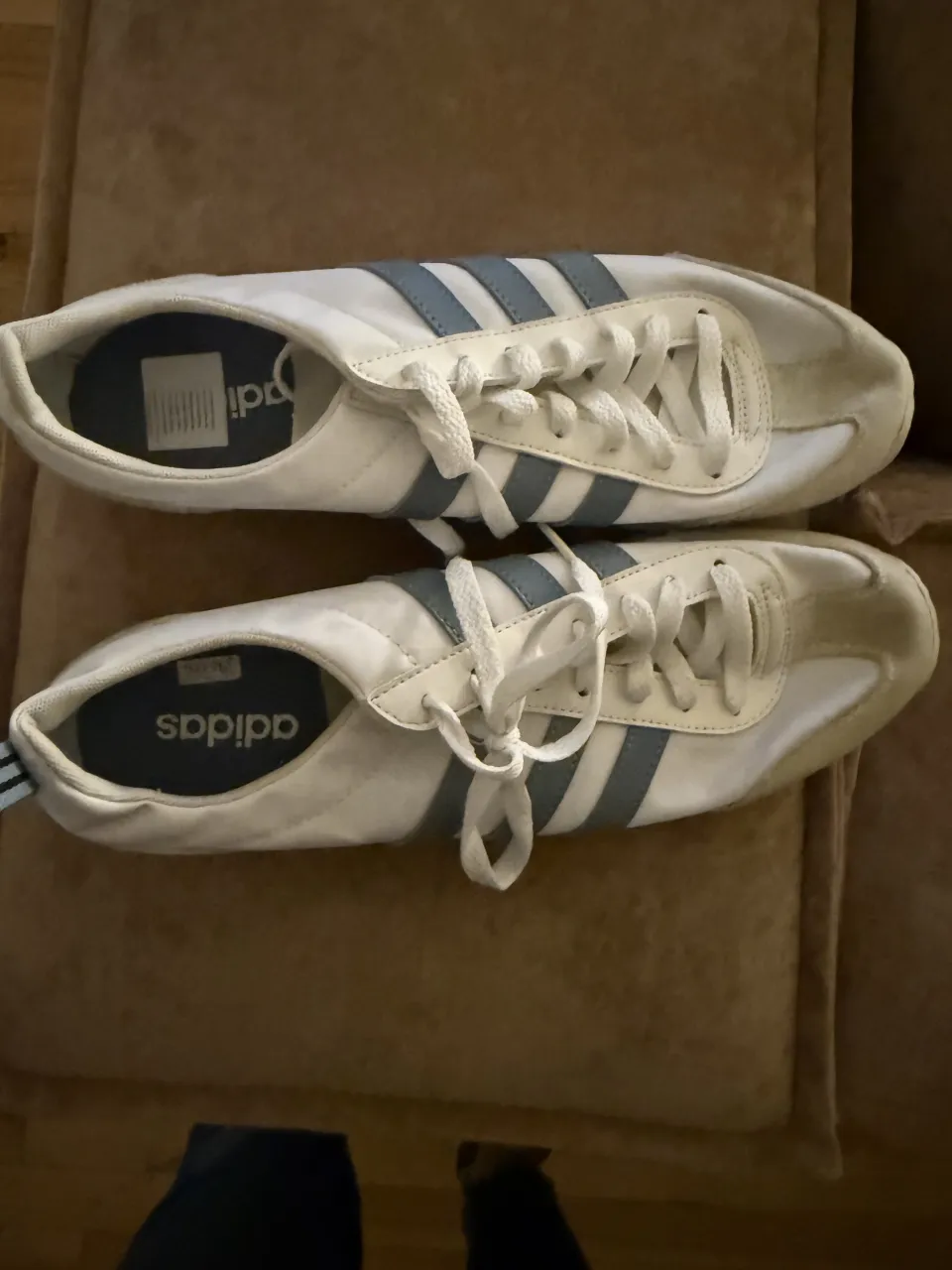 Zapatillas deportivas blancas con detalles en azul claro y cordones blancos.