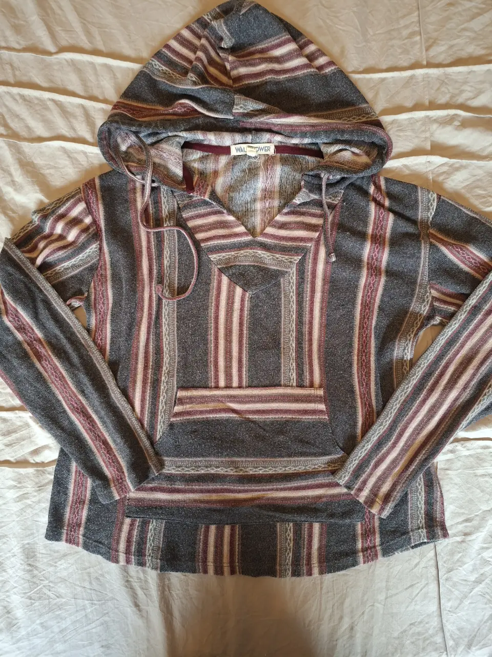 Buzo canguro con capucha, diseño a rayas en tonos grises, borgoña y blanco. Estilo boho y artesanal, ideal para un look casual y cómodo.