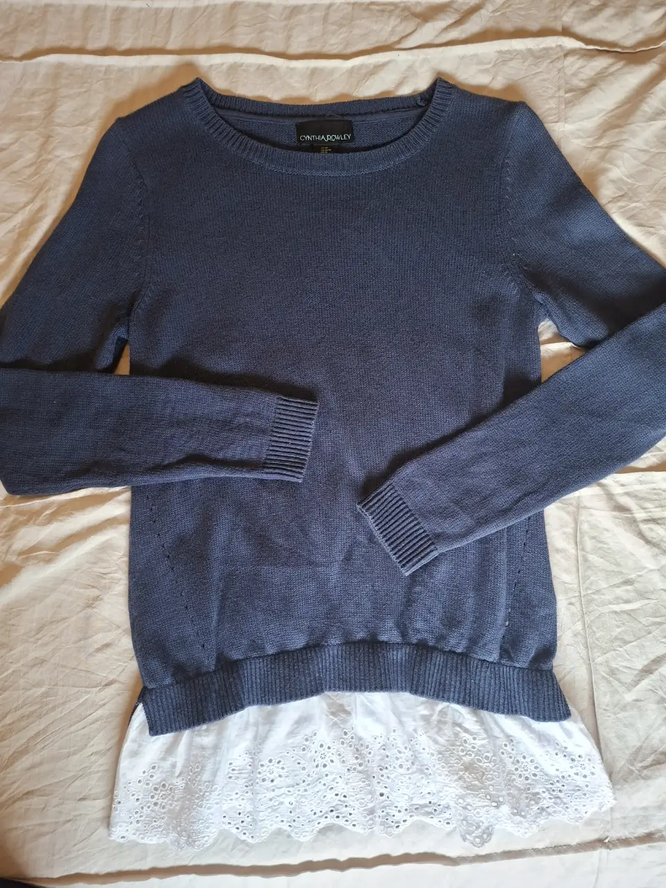 Sweater de mujer azul marino con detalle de volado blanco en el bajo. Cuello redondo y mangas largas. Ideal para un look casual y elegante.
