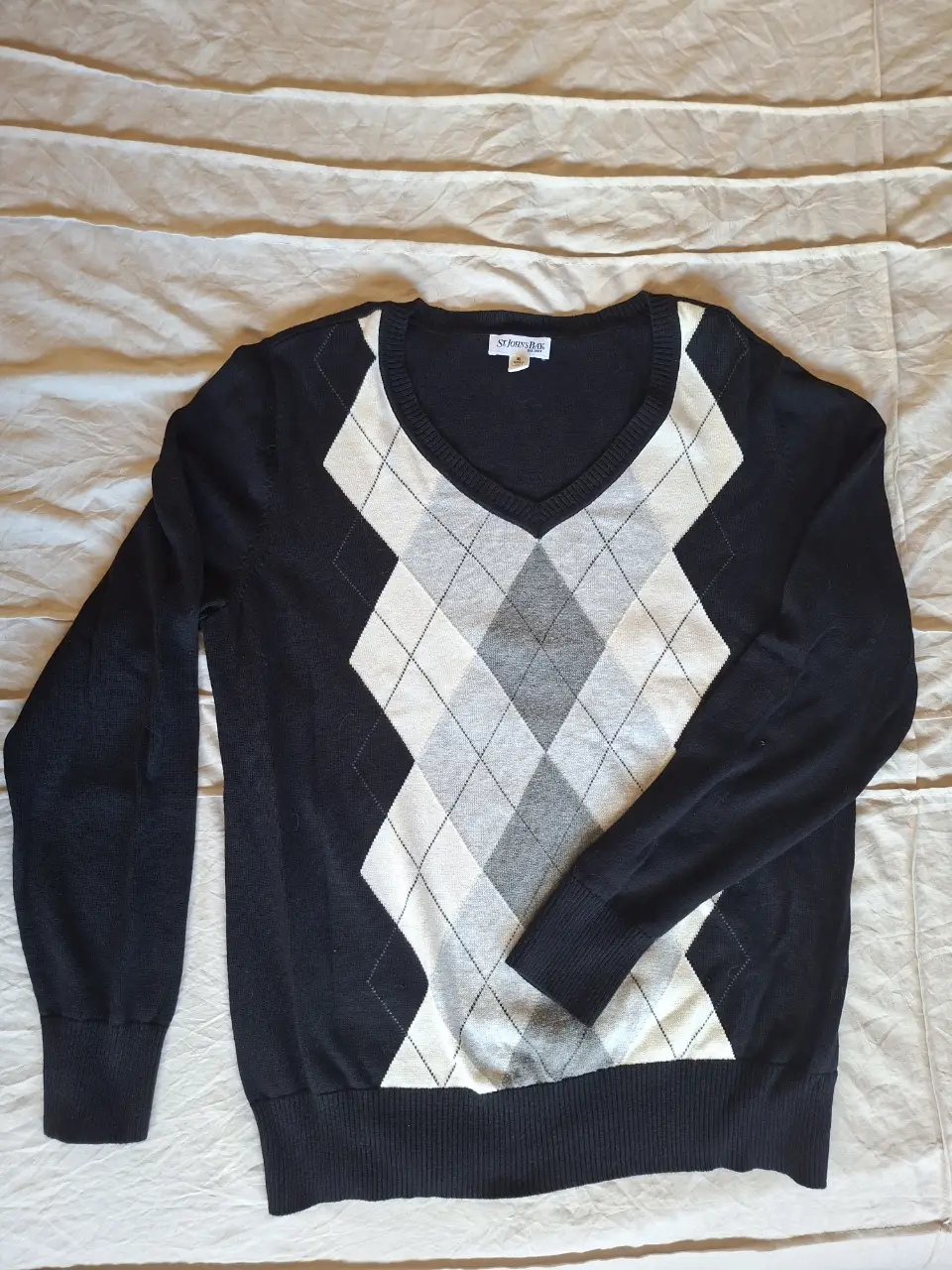 Clásico sweater en V con diseño de rombos en blanco, gris y negro. Ideal para un look preppy y elegante.