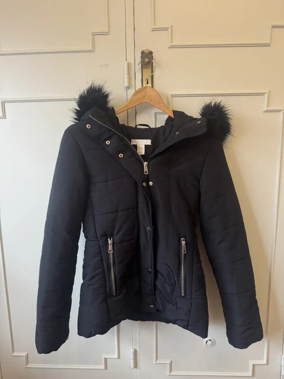 Campera negra acolchada con capucha y borde de piel sintética. Tiene cierre y bolsillos con cierre. Ideal para el invierno. talle S